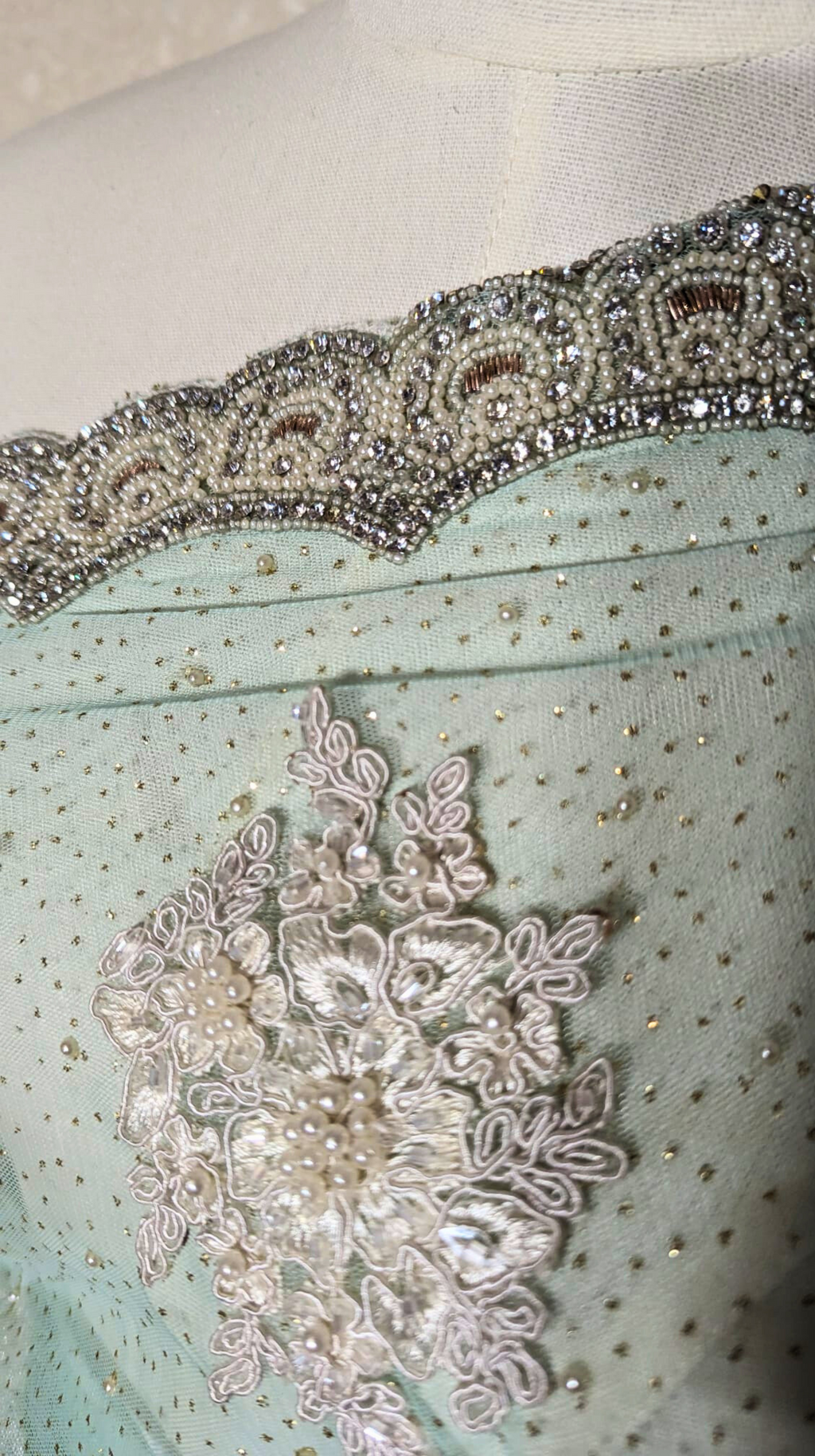 Close-up of decorative fabric with lace and beadwork on a light blue background.