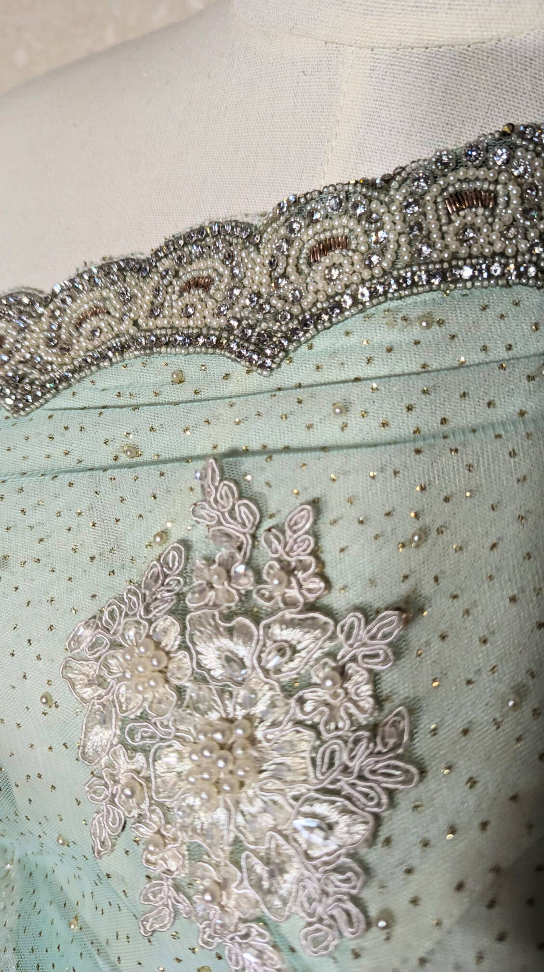 Close-up of decorative fabric with lace and beadwork on a light blue background.