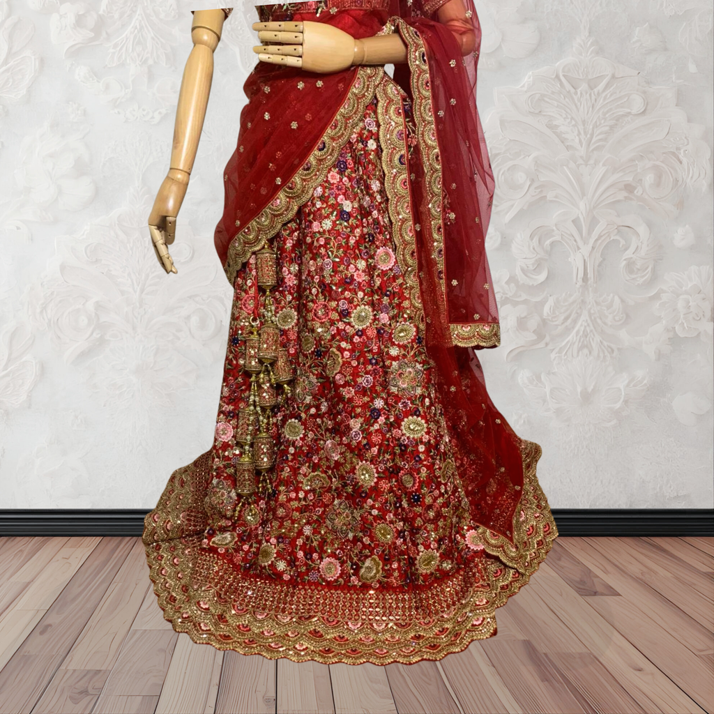 This exquisite red lehenga choli crafted from luxurious raw silk showcases intricate resham, zardosi, beads, sequins, and cut dana floral embroidery. The heavily embellished hemline and delicate cream butti accents enhance its sophisticated charm. Complete with a matching embroidered net dupatta featuring floral buttis and an elegant border, and a stitched blouse piece adorned with coordinating floral motifs, for wedding and bridal, pakistani, bangladeshi, indian, sri lankan.