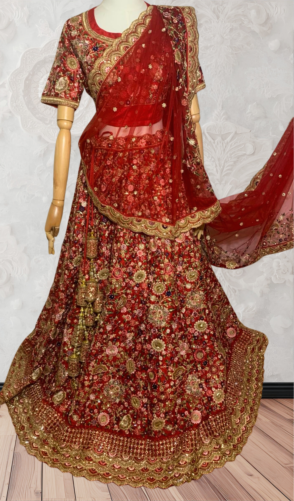 This exquisite red lehenga choli crafted from luxurious raw silk showcases intricate resham, zardosi, beads, sequins, and cut dana floral embroidery. The heavily embellished hemline and delicate cream butti accents enhance its sophisticated charm. Complete with a matching embroidered net dupatta featuring floral buttis and an elegant border, and a stitched blouse piece adorned with coordinating floral motifs, for wedding and bridal, pakistani, bangladeshi, indian, sri lankan.