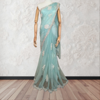 Teal saree with silver embroidery on a mannequin against a white textured wall.
