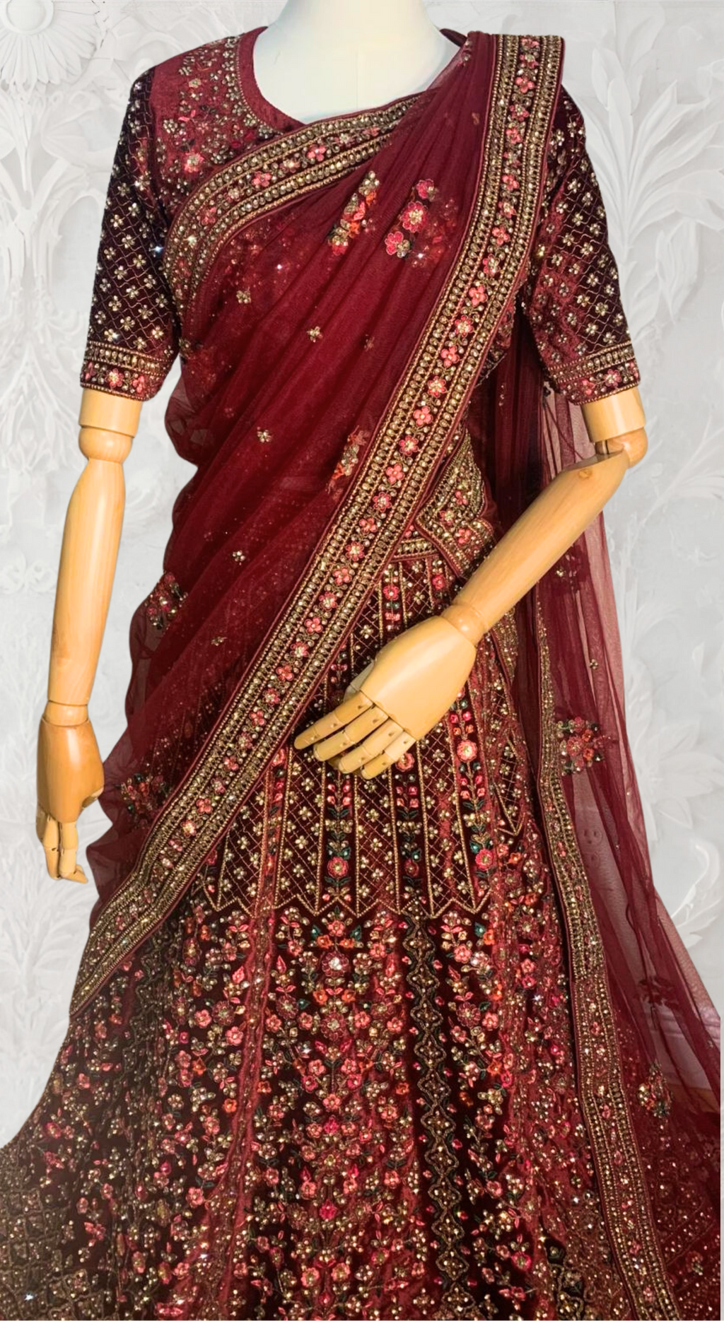 Maroon Lehenga with gold embroidery on a mannequin against a white wall. traditional desi, Indian, Pakistani, Bangladeshi, Sri lankan bridal ware for wedding. 