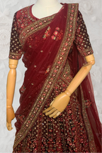 Maroon Lehenga with gold embroidery on a mannequin against a white wall. traditional desi, Indian, Pakistani, Bangladeshi, Sri lankan bridal ware for wedding. 