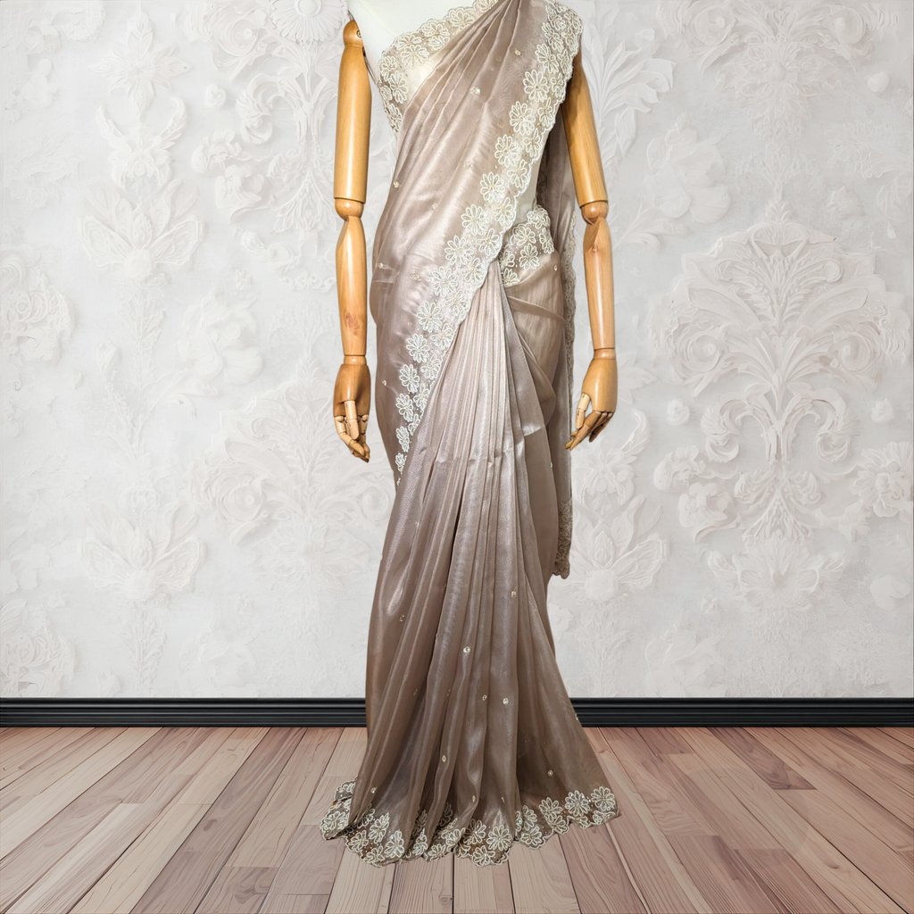 Mannequin wearing a beige saree with lace details on a wooden floor and white wall background