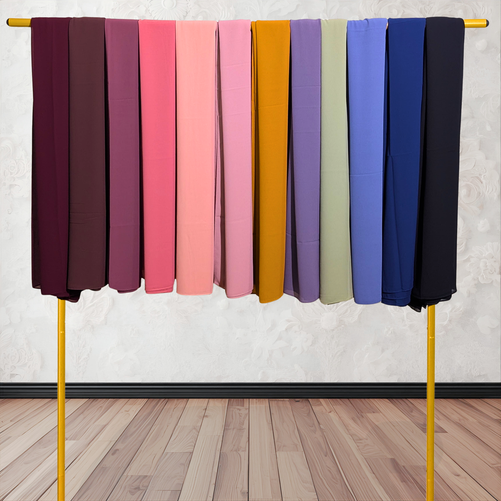 Row of colorful fabrics hanging on a yellow rod against a white wall. Chiffon hijab
