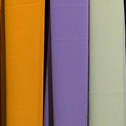 Row of colorful cloths hanging on a yellow rod against a white wall.