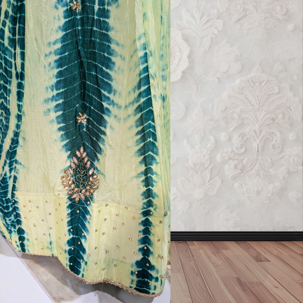 Green and yellow tie-dye fabric with intricate patterns on a textured white wall.