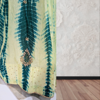 Green and yellow tie-dye fabric with intricate patterns on a textured white wall.