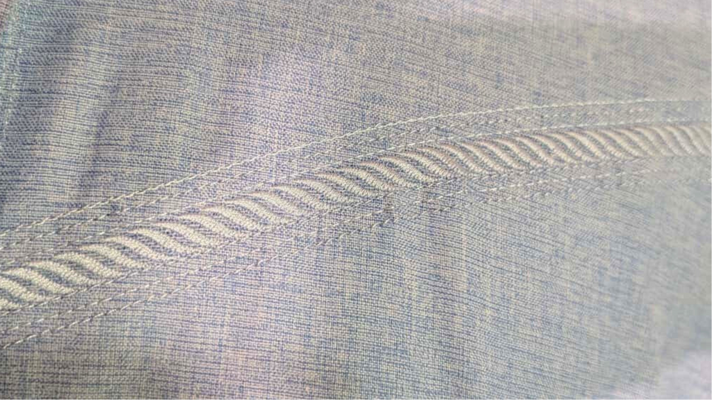 Blue denim shirt on a mannequin with close-up of stitching detail on a beige background