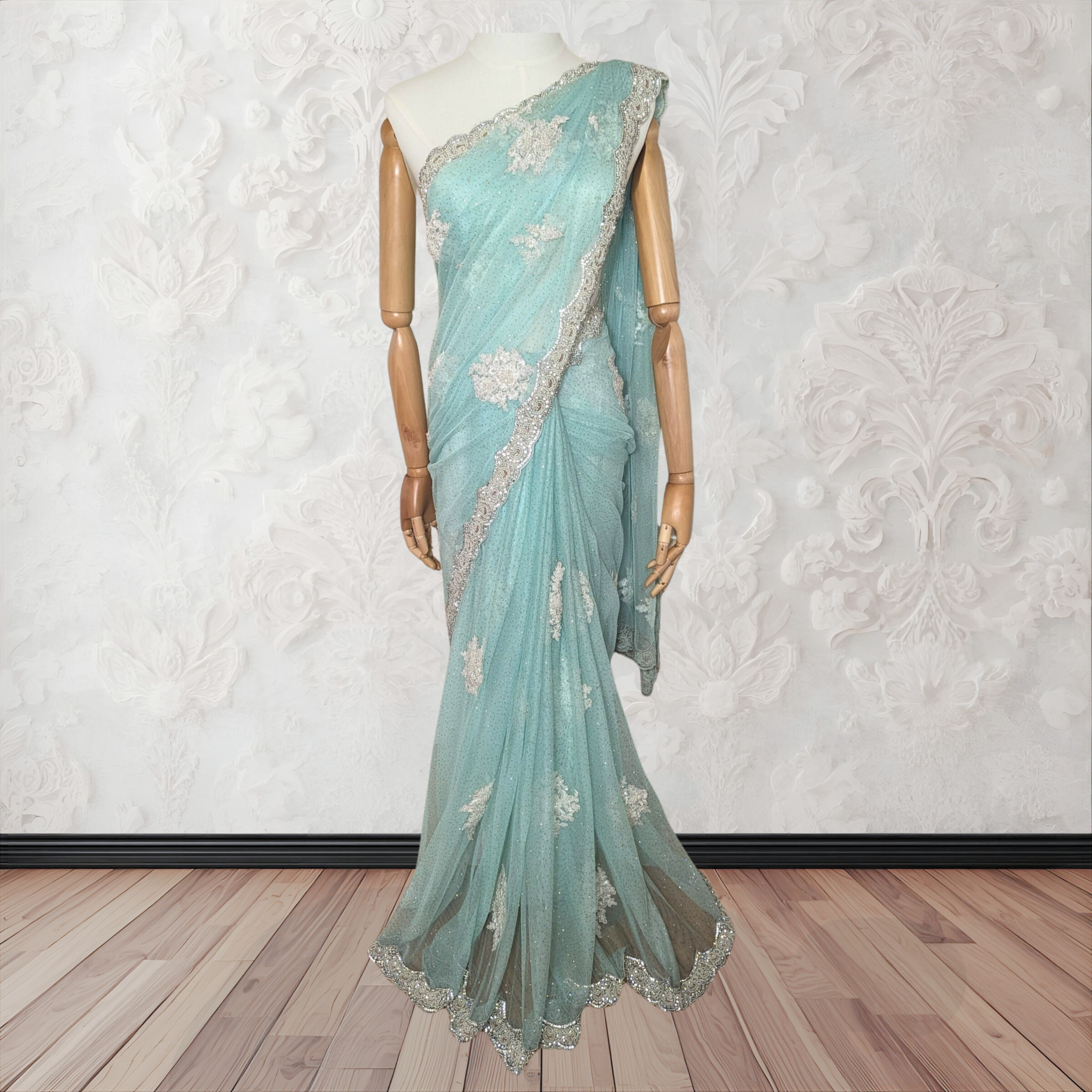 Light blue saree with white floral embroidery on a mannequin against a white wall.