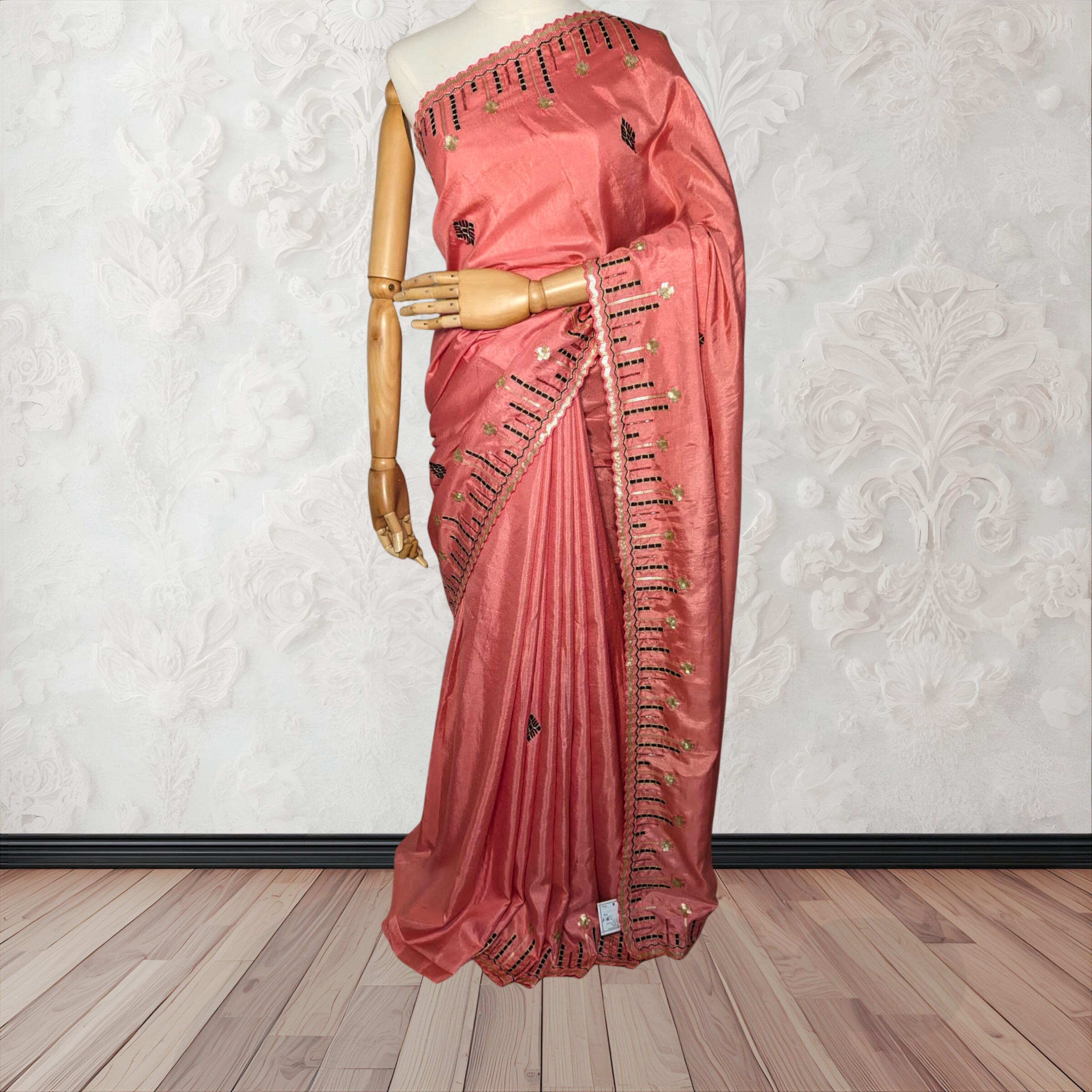 Pink saree with black embroidery on a mannequin against a white wall.