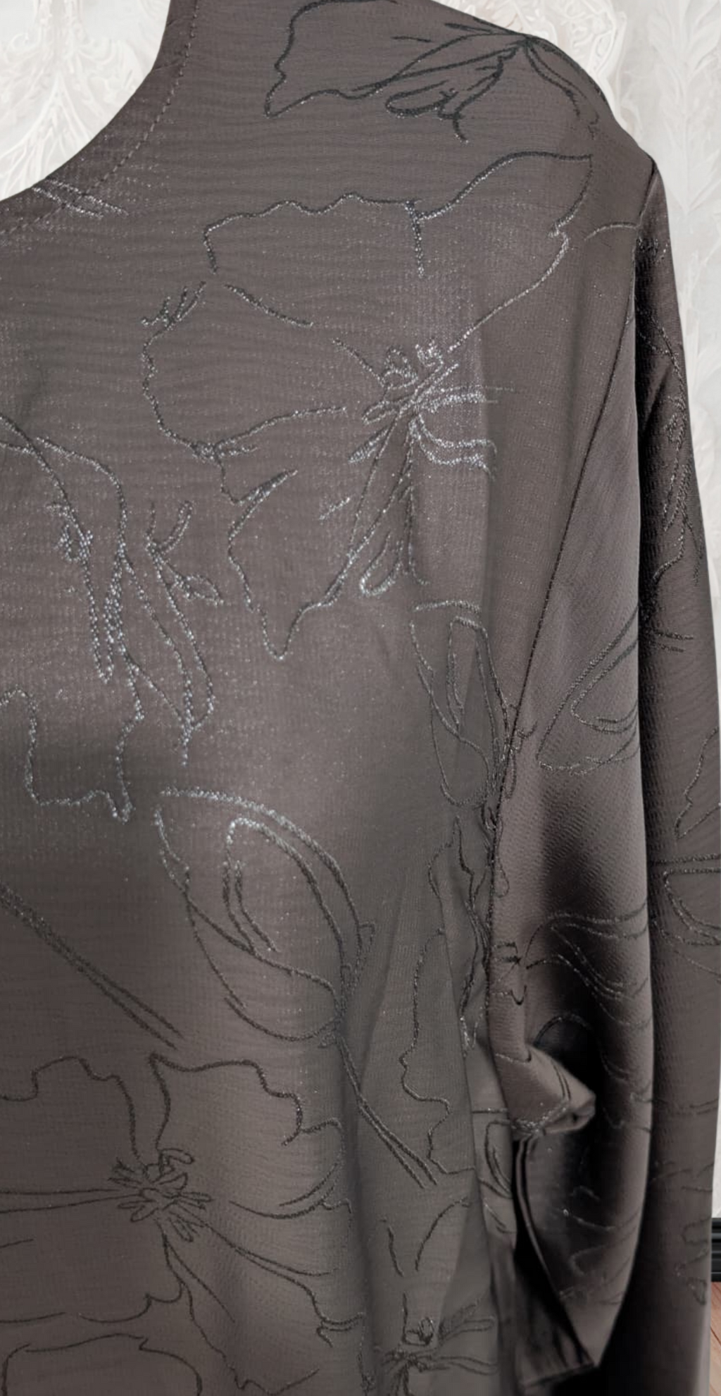 Brown floral-patterned fabric draped over a mannequin against a decorative wall.