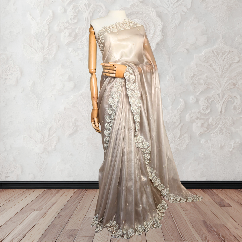 Mannequin wearing a beige saree with floral lace details against a decorative wall.