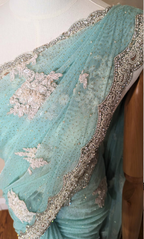 Close-up of a turquoise saree with silver embroidery on a wooden surface.