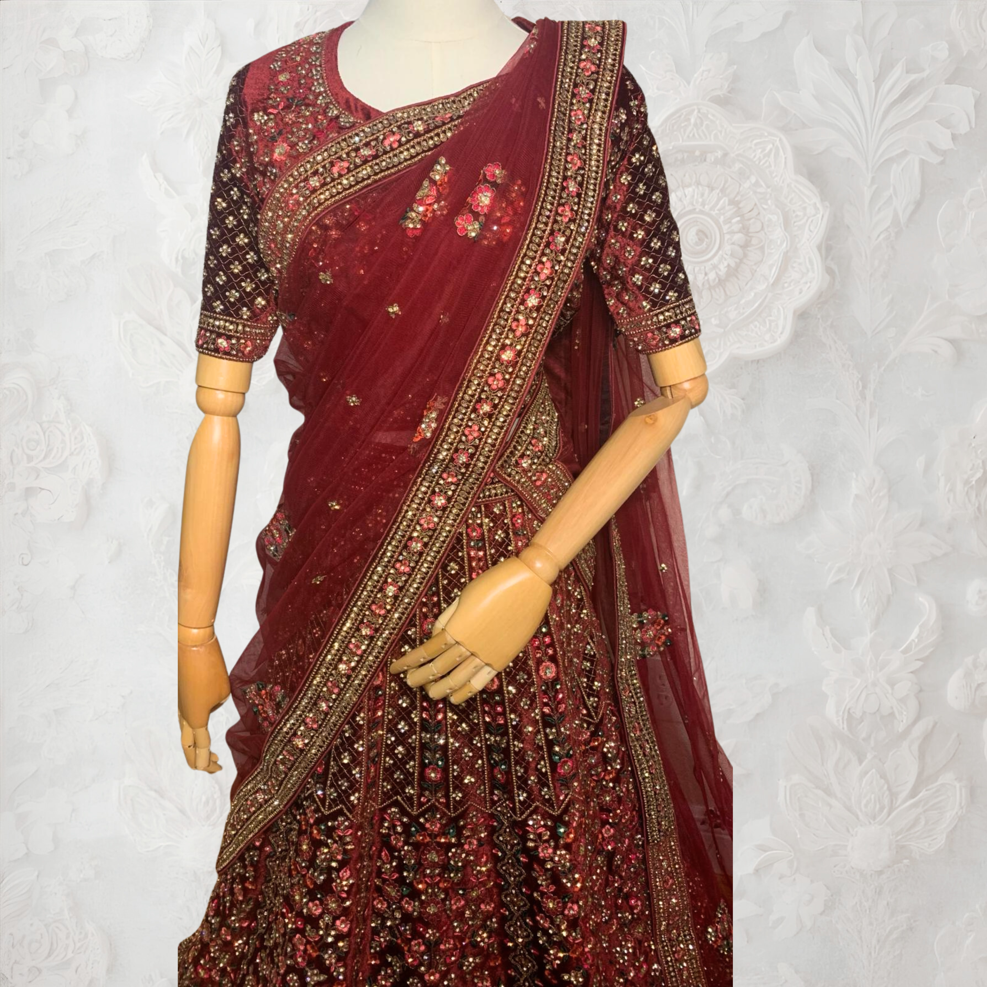 Maroon Lehenga with gold embroidery on a mannequin against a white wall. traditional desi, indian bridal ware for wedding. 