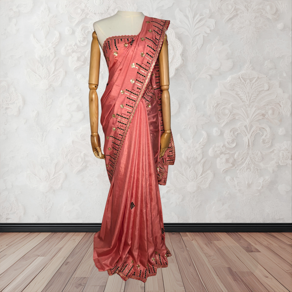Pink saree with gold embroidery on a mannequin against a white textured wall.