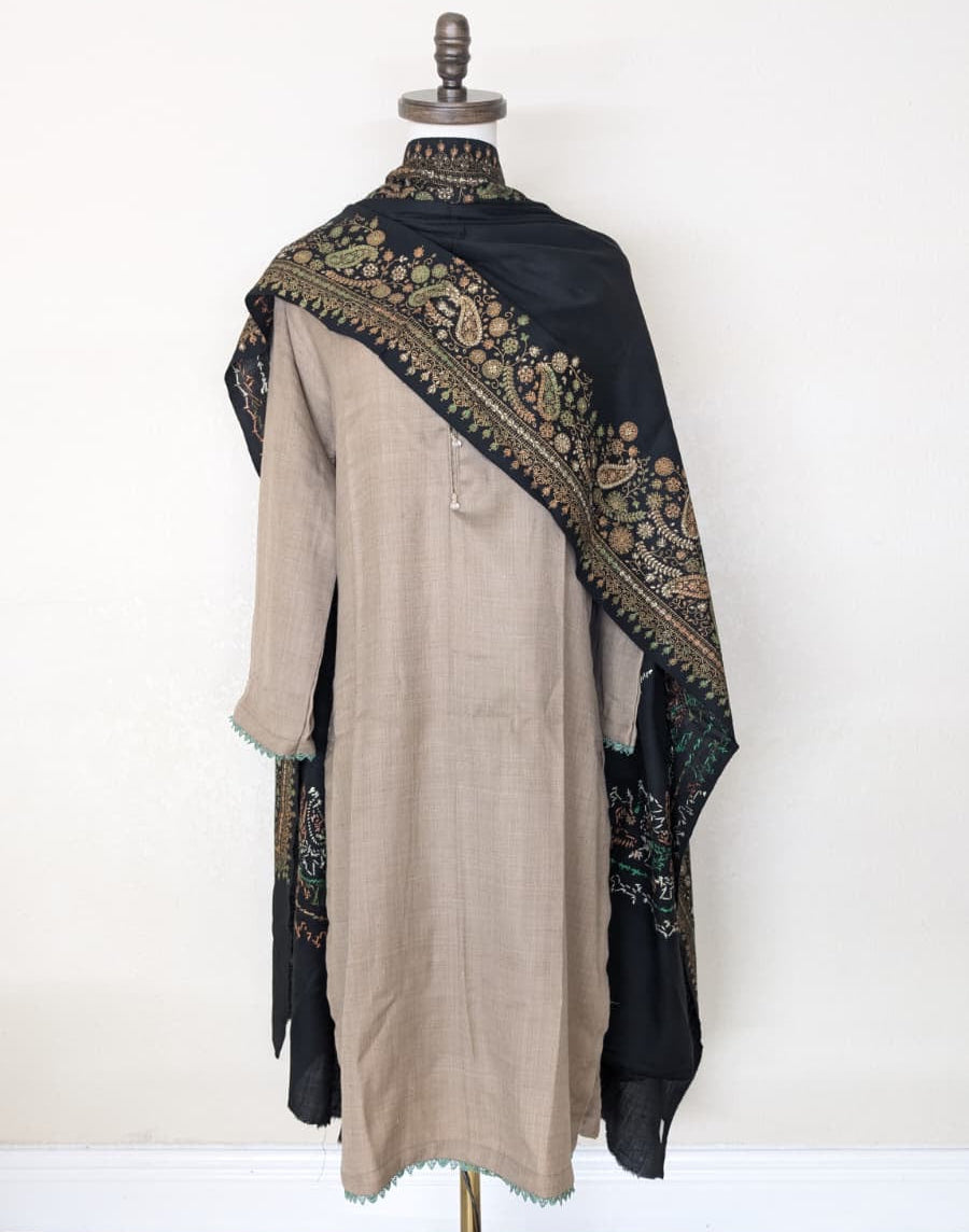 Mannequin wearing a beige outfit with a black embroidered shawl on a white background