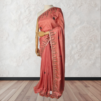 Pink saree with intricate designs on a mannequin against a white textured wall.
