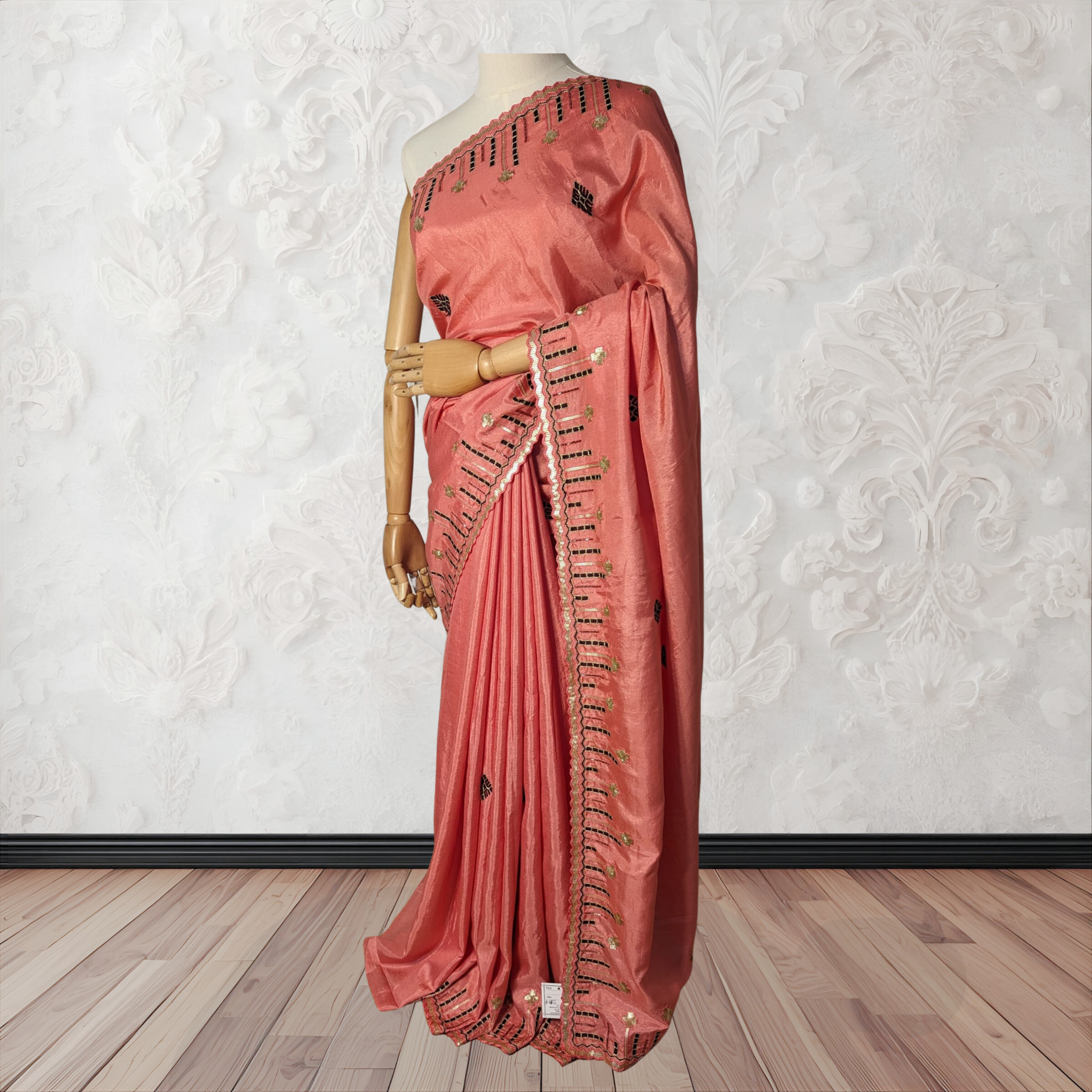 Pink saree with intricate designs on a mannequin against a white textured wall.