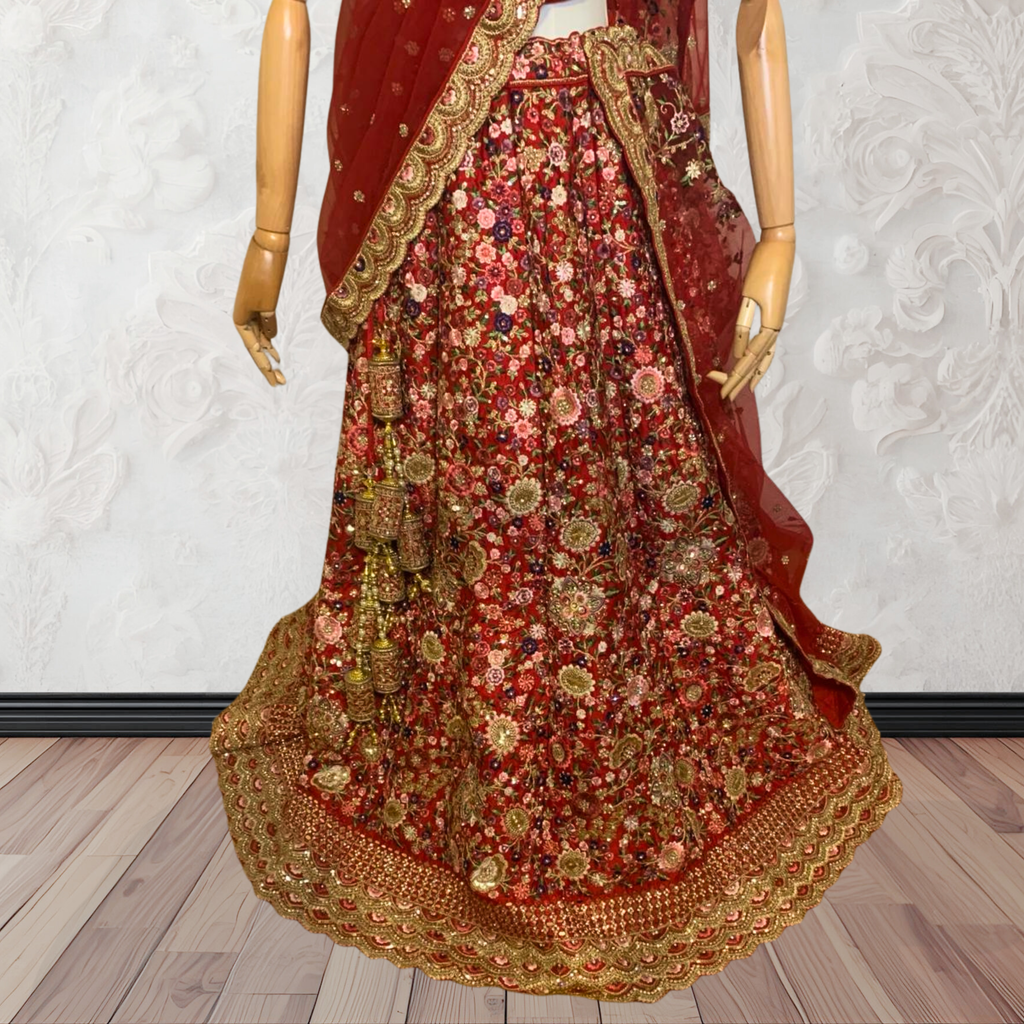This exquisite red lehenga choli crafted from luxurious raw silk showcases intricate resham, zardosi, beads, sequins, and cut dana floral embroidery. The heavily embellished hemline and delicate cream butti accents enhance its sophisticated charm. Complete with a matching embroidered net dupatta featuring floral buttis and an elegant border, and a stitched blouse piece adorned with coordinating floral motifs, for wedding and bridal, pakistani, bangladeshi, indian, sri lankan.