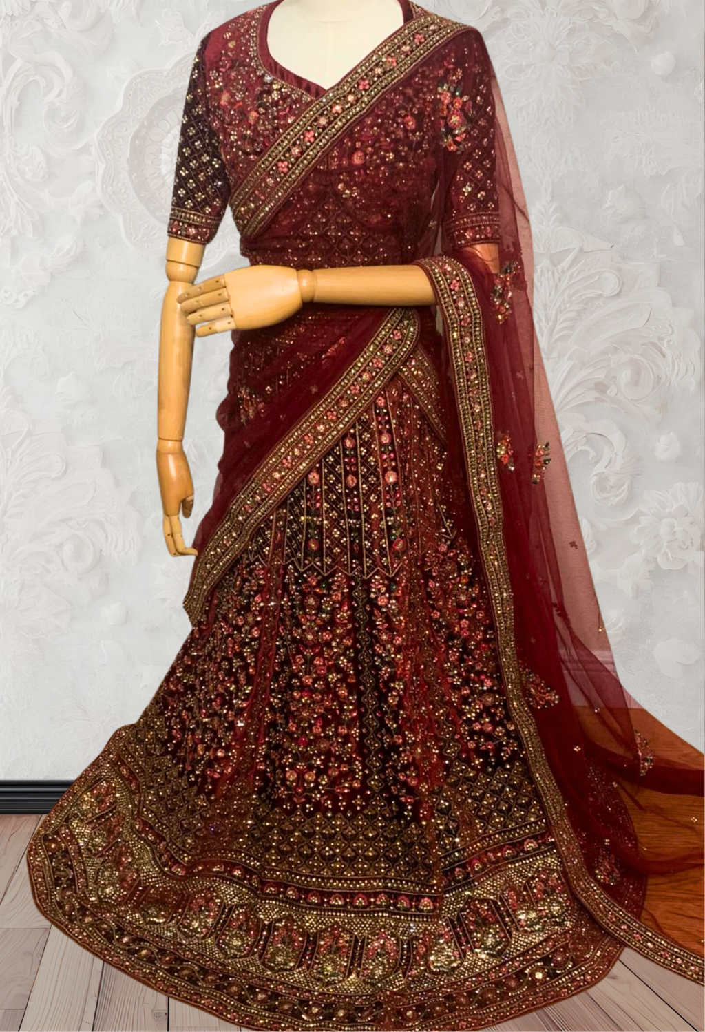 Maroon Lehenga with gold embroidery on a mannequin against a white wall. traditional desi, indian bridal ware for wedding. 