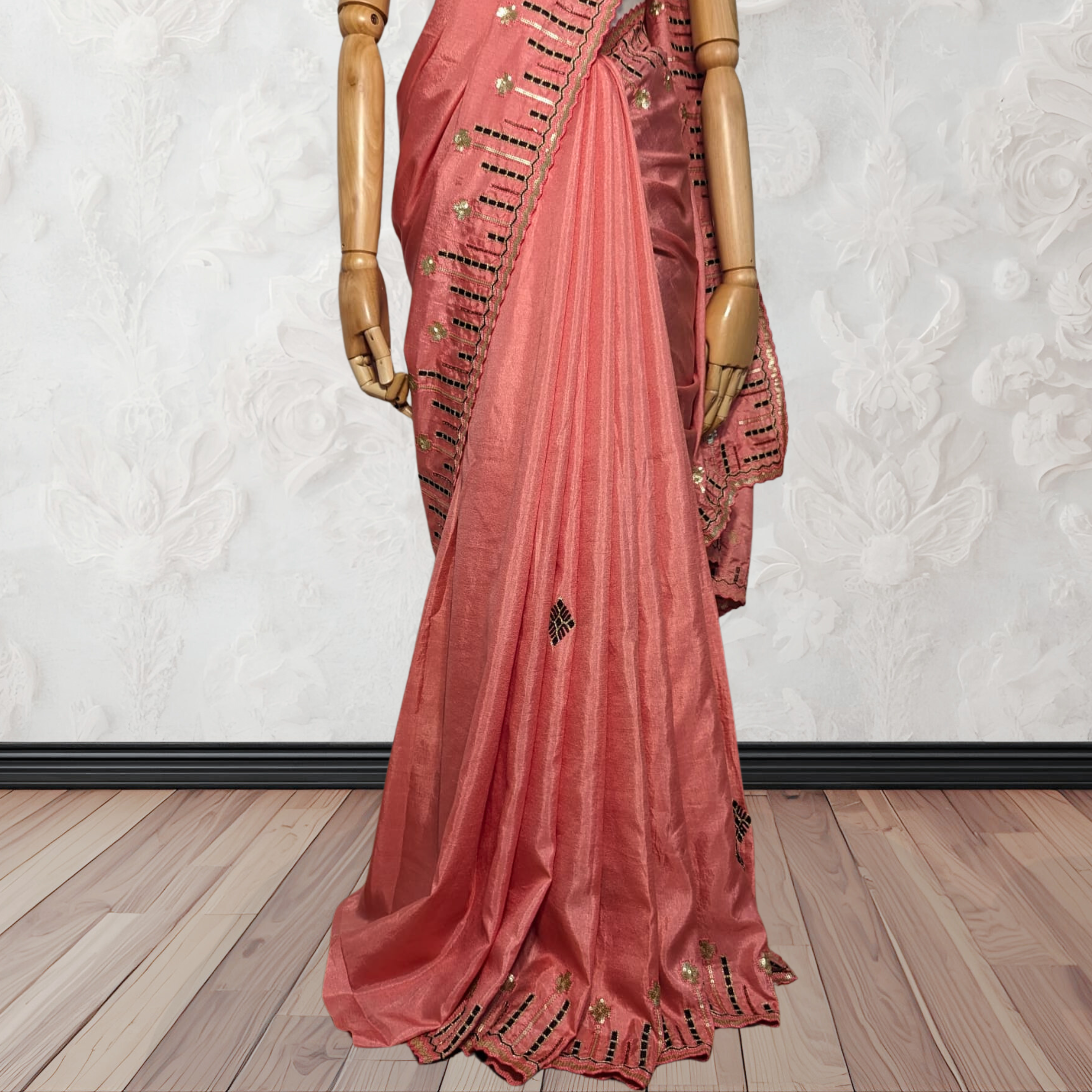 Pink saree with gold embroidery on a wooden floor against a white wall