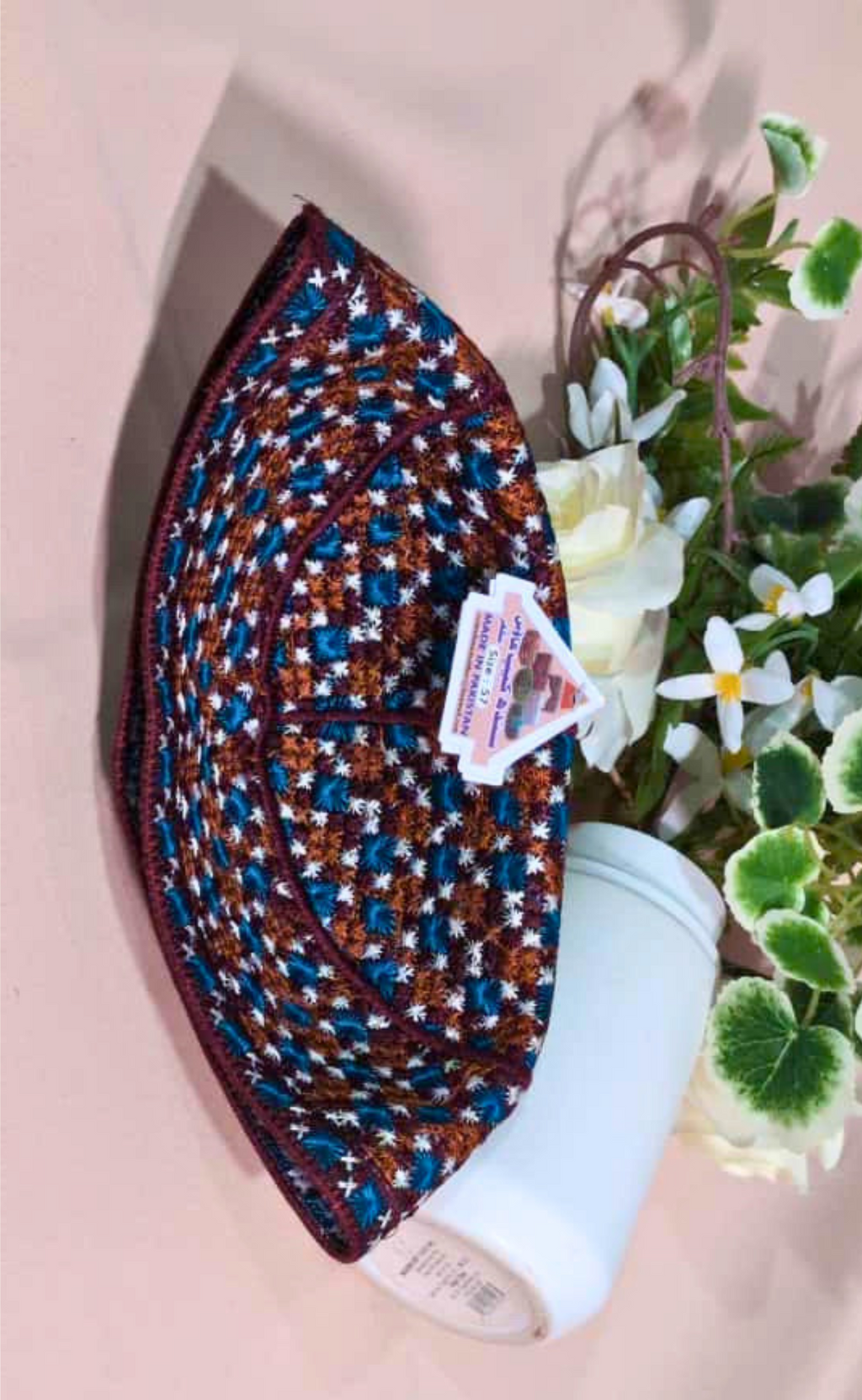 Colorful woven mat with a white bottle underneath, on a light pink background with flowers.