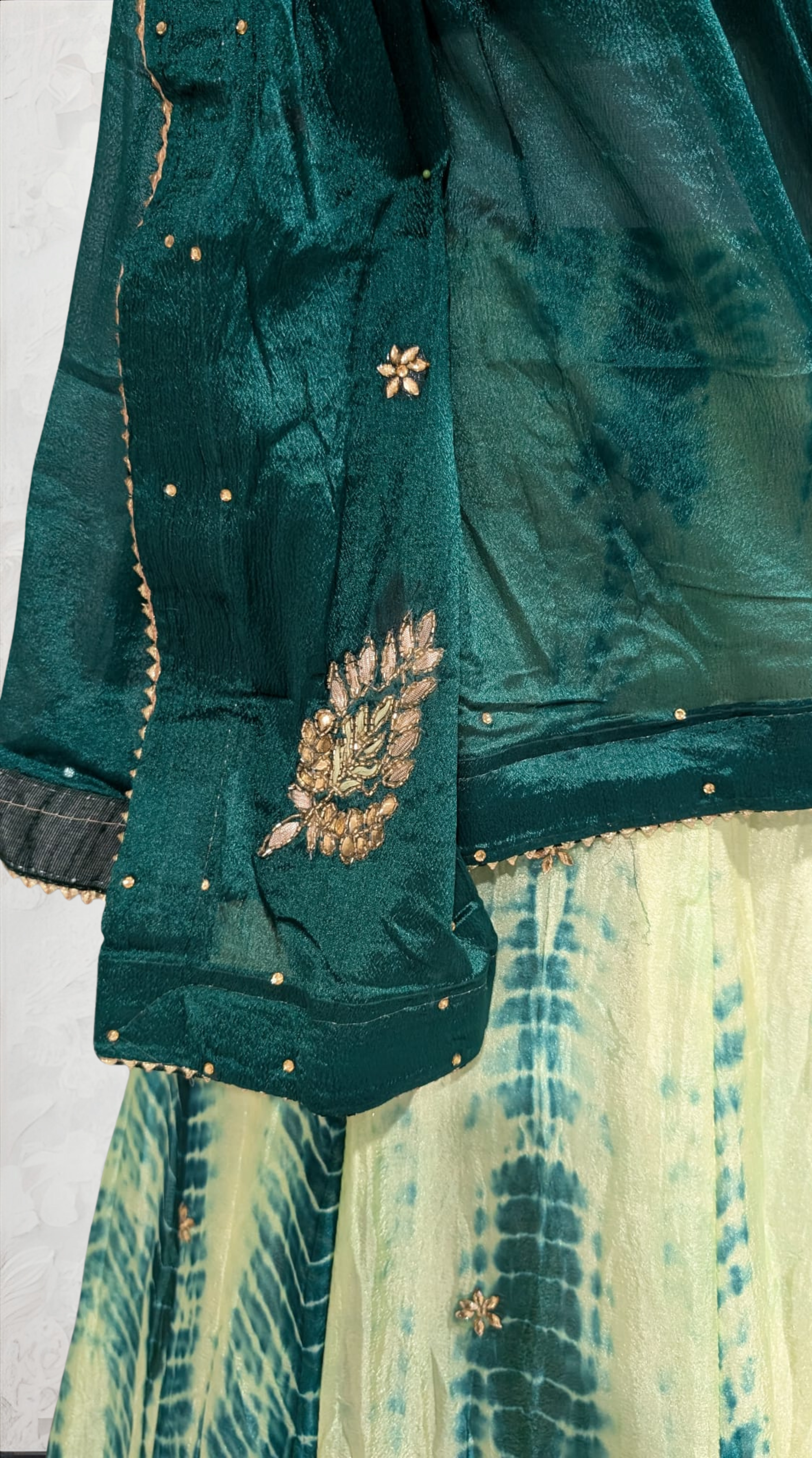 Green embroidered garment with a white floral design on a textured white background