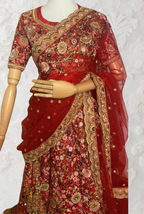 This exquisite red lehenga choli crafted from luxurious raw silk showcases intricate resham, zardosi, beads, sequins, and cut dana floral embroidery. The heavily embellished hemline and delicate cream butti accents enhance its sophisticated charm. Complete with a matching embroidered net dupatta featuring floral buttis and an elegant border, and a stitched blouse piece adorned with coordinating floral motifs, for wedding and bridal, pakistani, bangladeshi, indian, sri lankan.