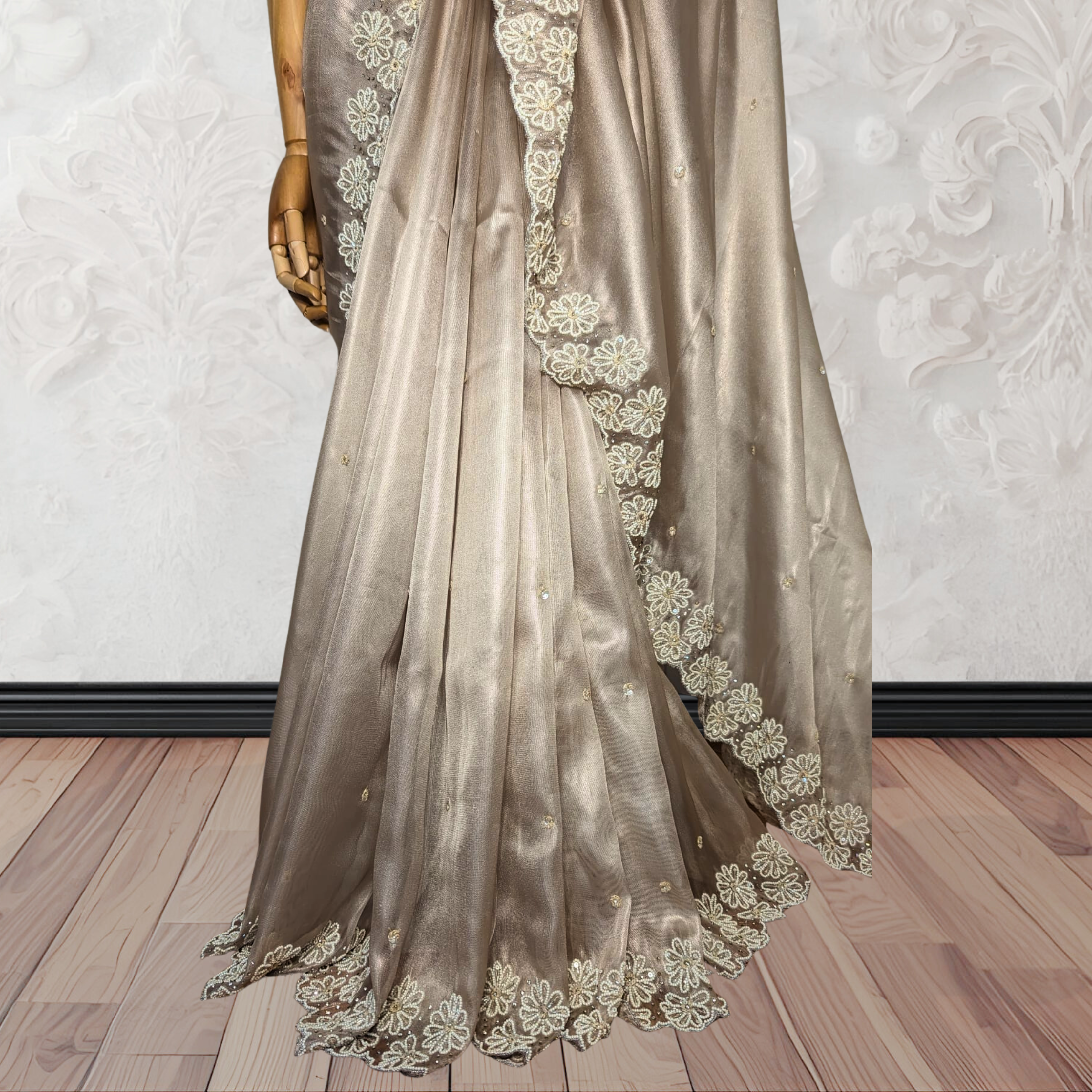 Brown saree with floral embroidery on a wooden floor against a white wall.