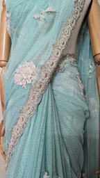Light blue saree with silver embroidery on a mannequin against a white textured wall.