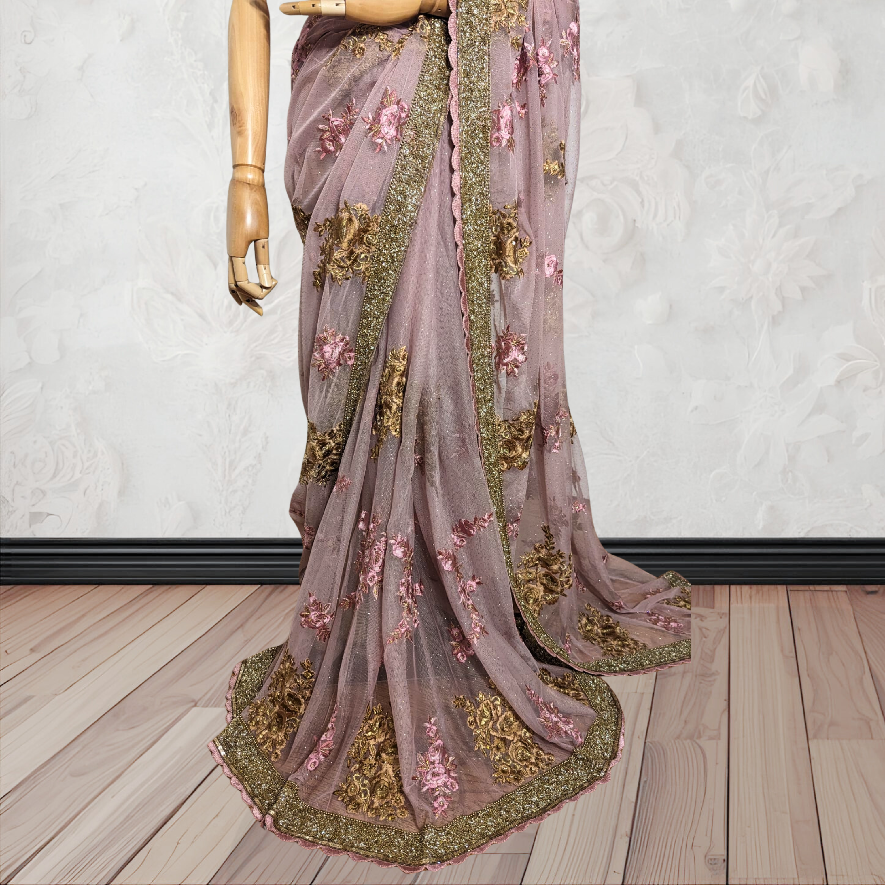 Decorative saree with floral and gold embroidery on a mannequin against a white wall.