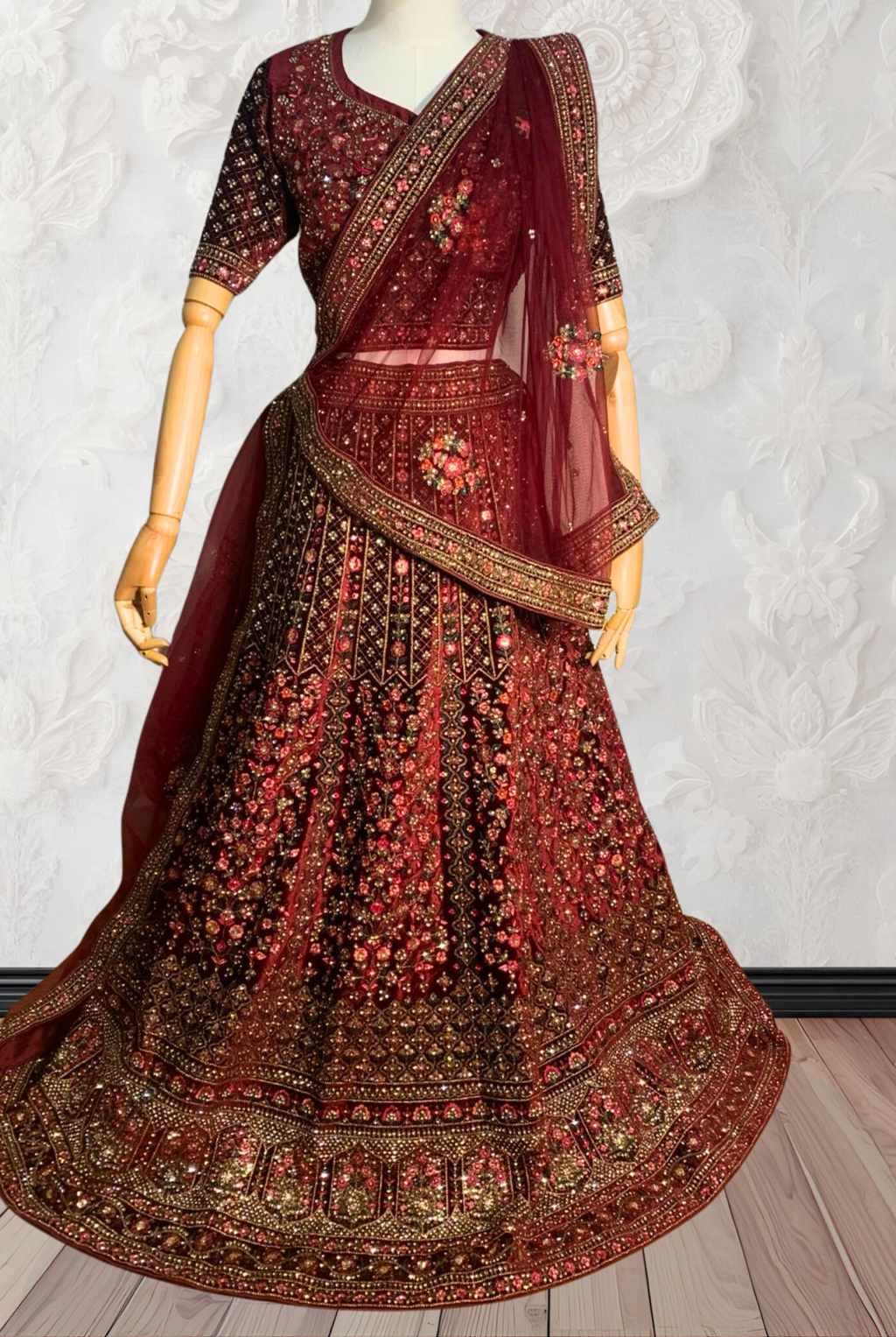 Maroon Lehenga with gold embroidery on a mannequin against a white wall. traditional desi, indian bridal ware for wedding. 