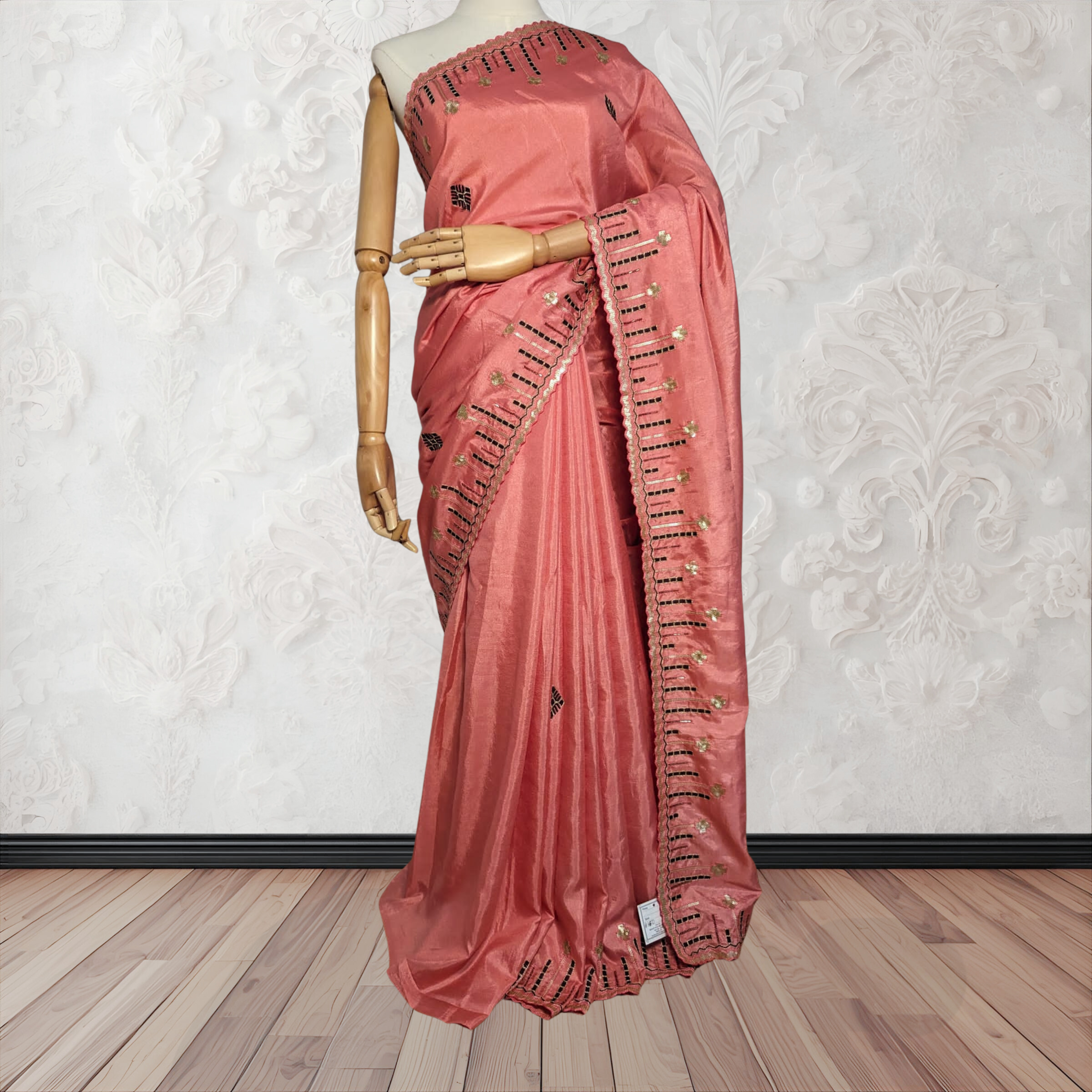 Pink saree with intricate designs on a mannequin against a white wall.