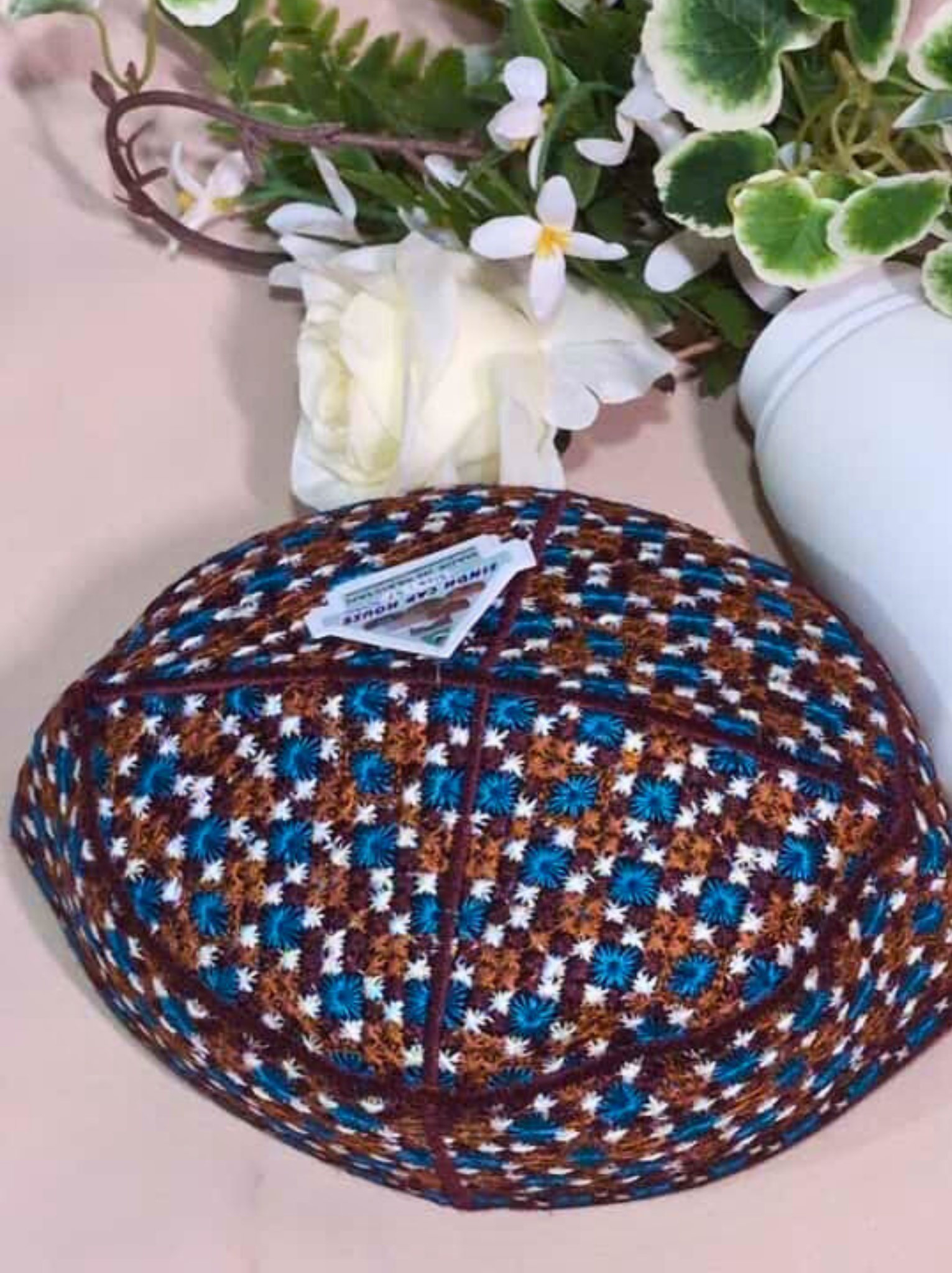 Woven fabric with a geometric pattern on a light pink surface, with a small plant in the background.