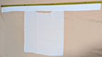 White fabric with a pocket on a beige background, with a measuring tape at the top.