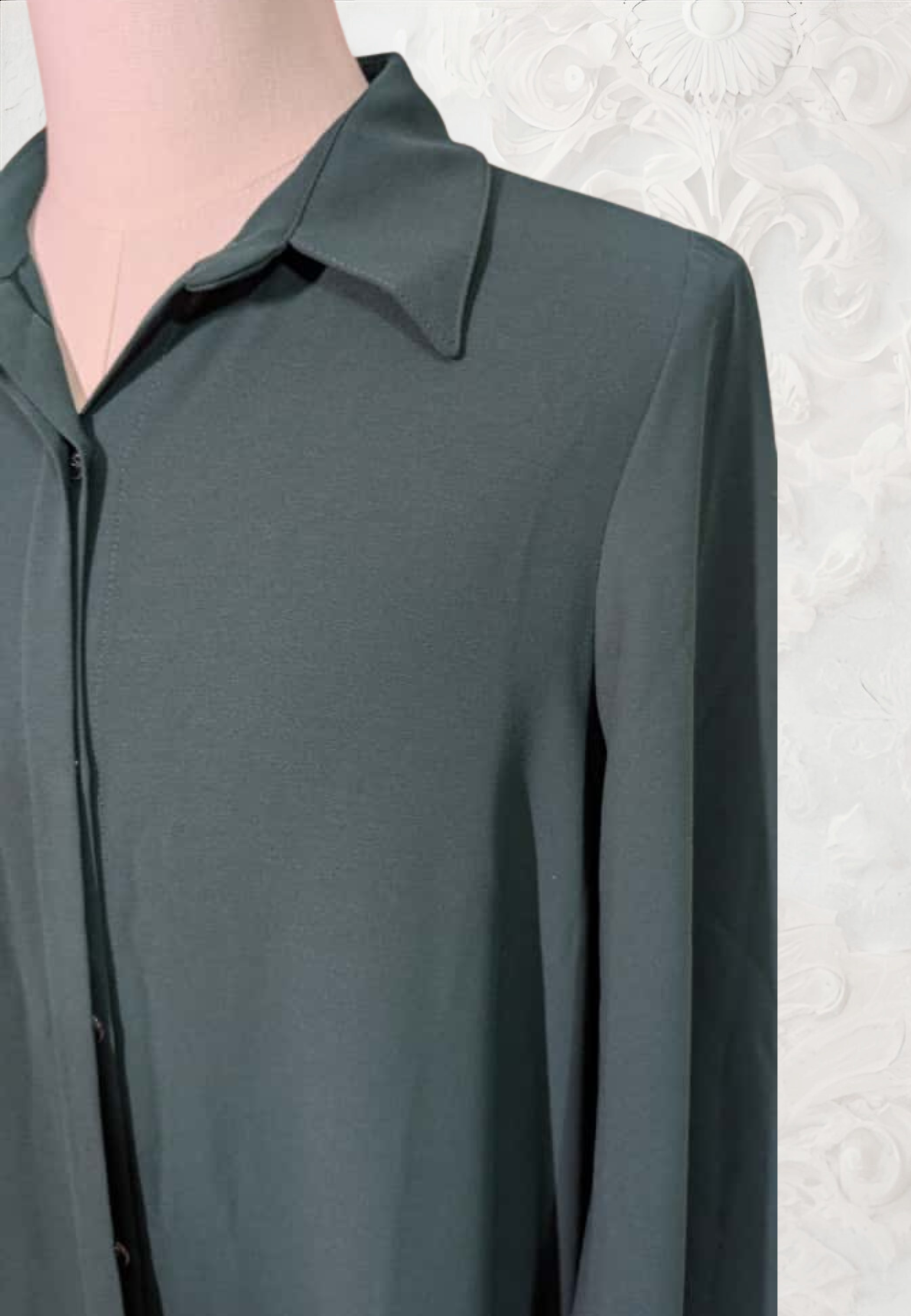 Mannequin wearing a dark gray shirt against a decorative white wall with wooden flooring.