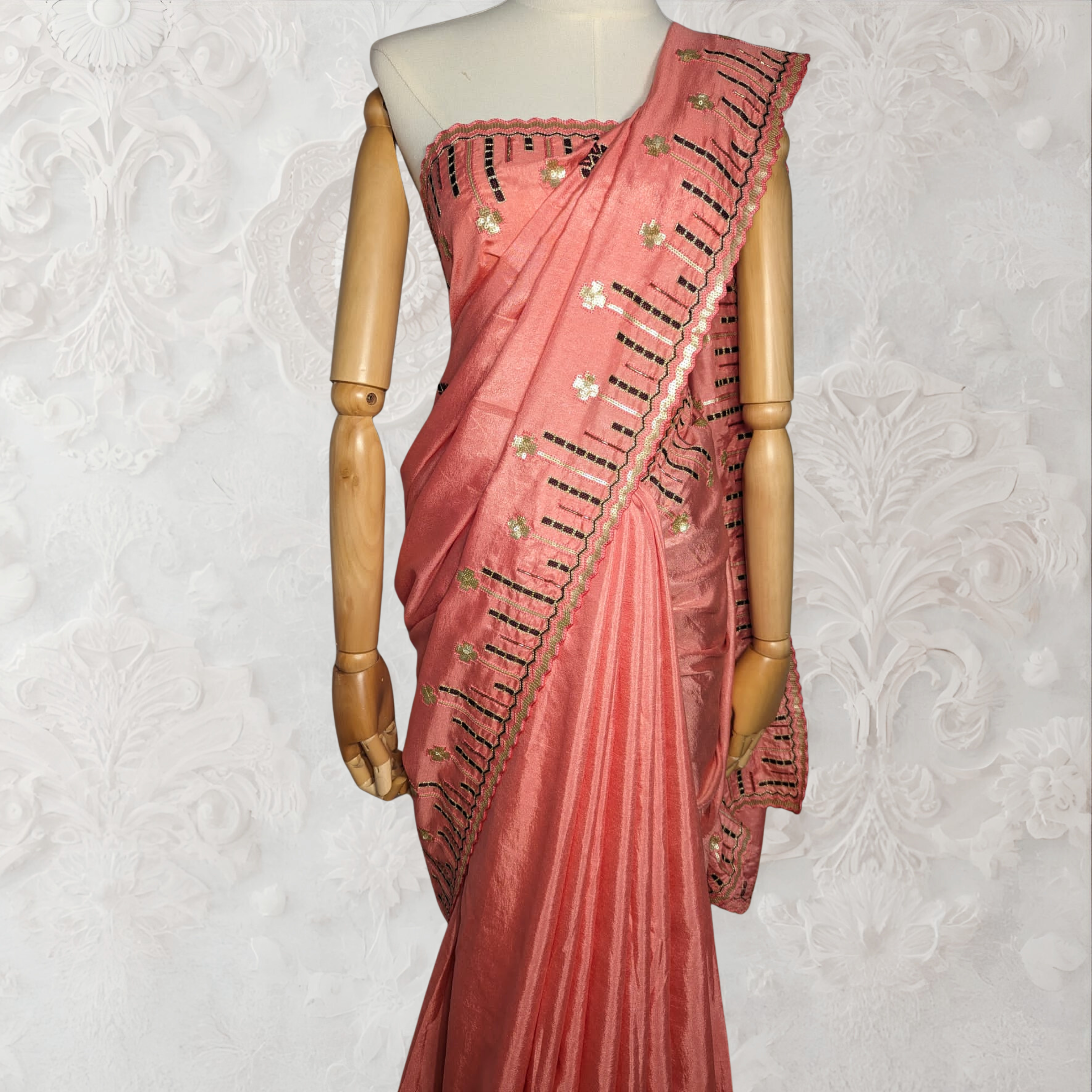 Coral saree with black embroidery on a mannequin against a white background