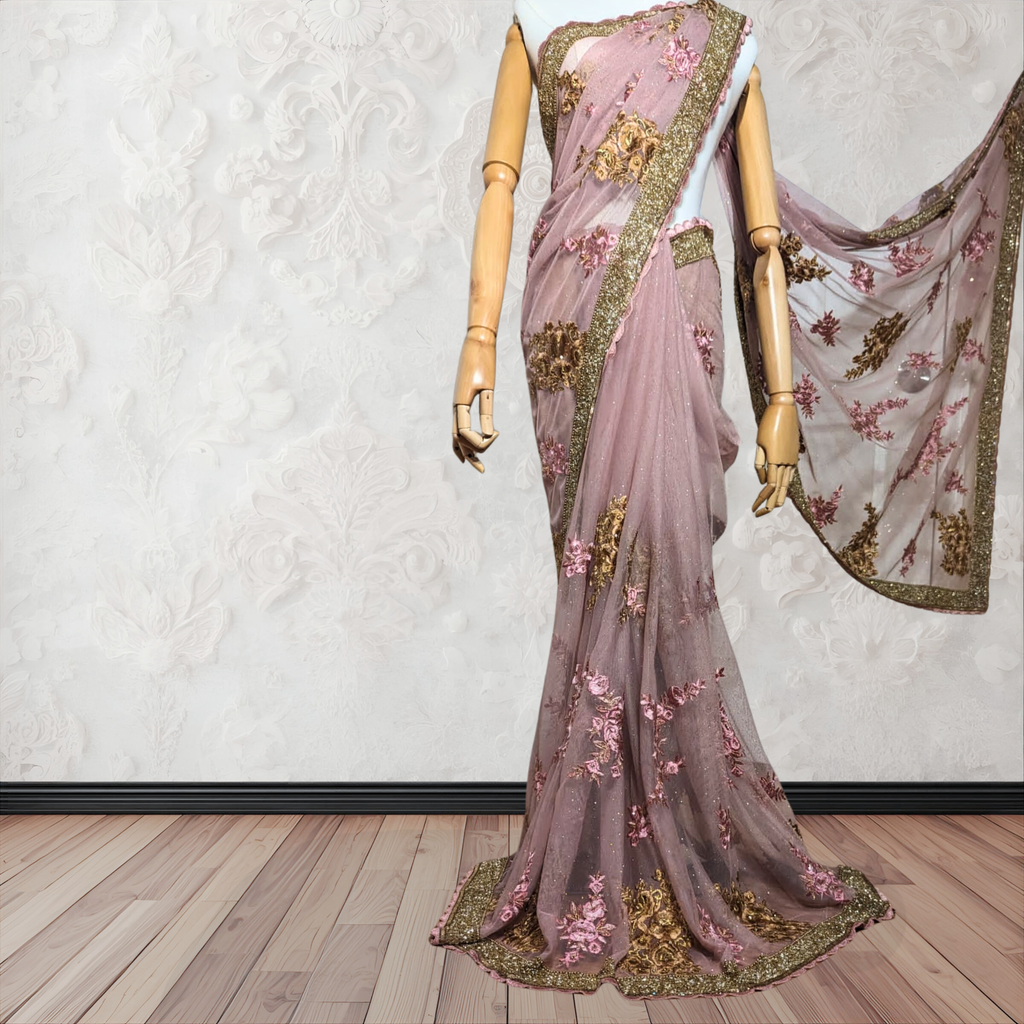 Pink saree with floral patterns and gold accents on a mannequin against a white wall.