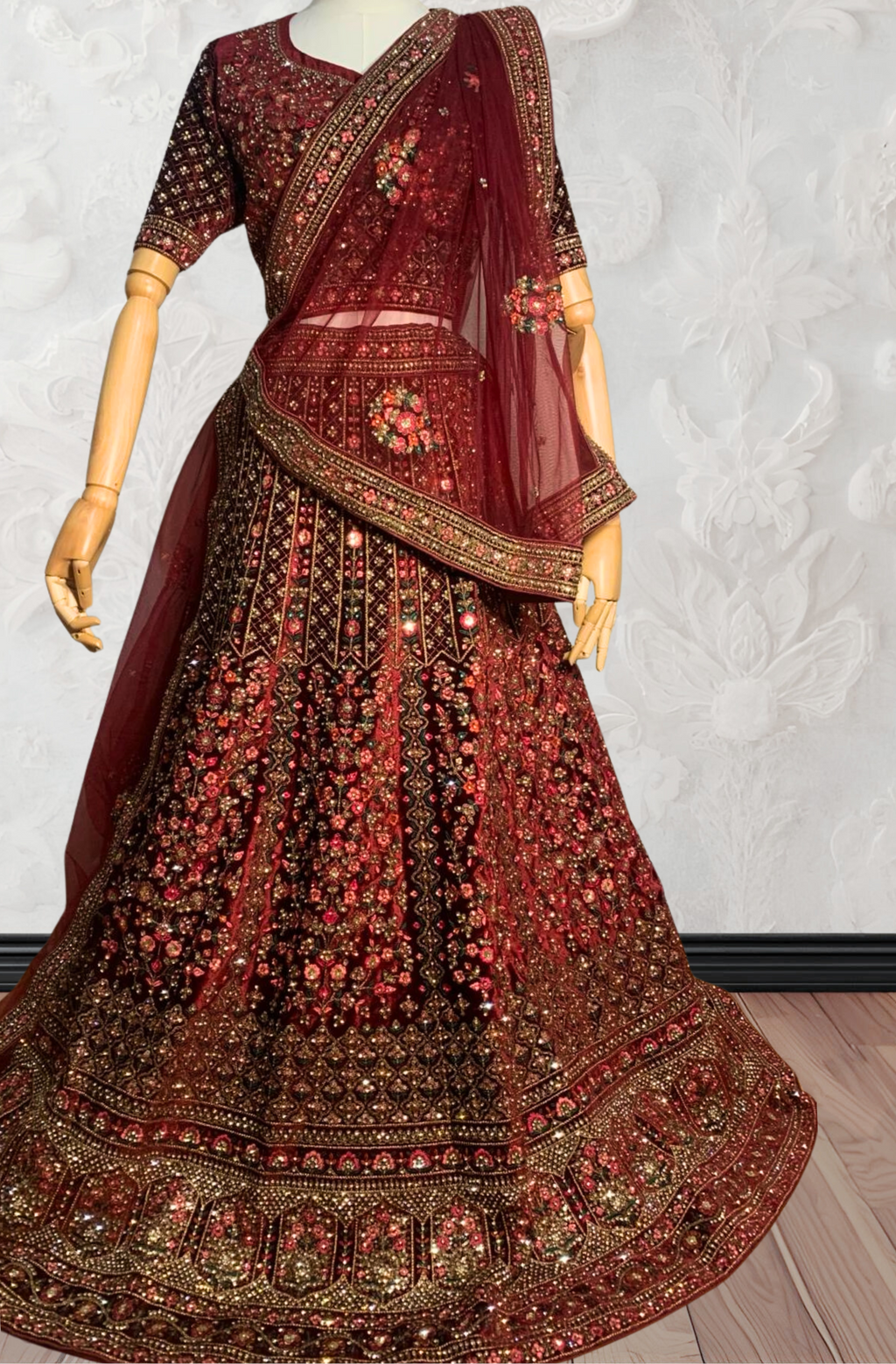 Maroon Lehenga with gold embroidery on a mannequin against a white wall. traditional desi, Indian, Pakistani, Bangladeshi, Sri lankan bridal ware for wedding. 