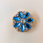 Decorative brooch with blue gemstones and gold accents on a beige background