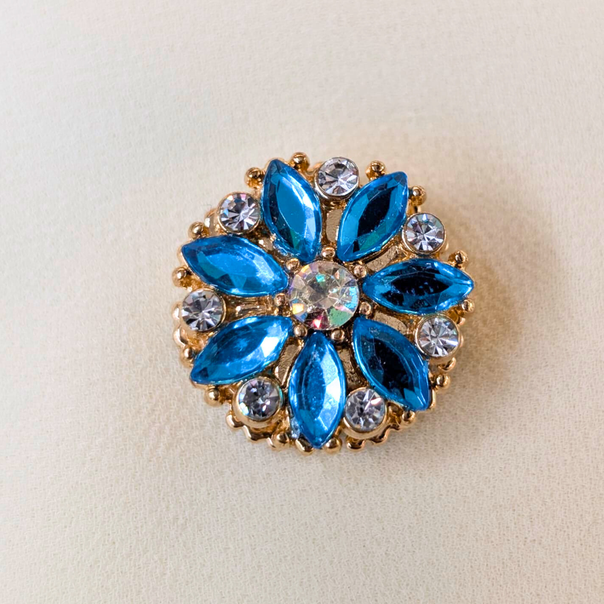 Decorative brooch with blue gemstones and gold accents on a beige background