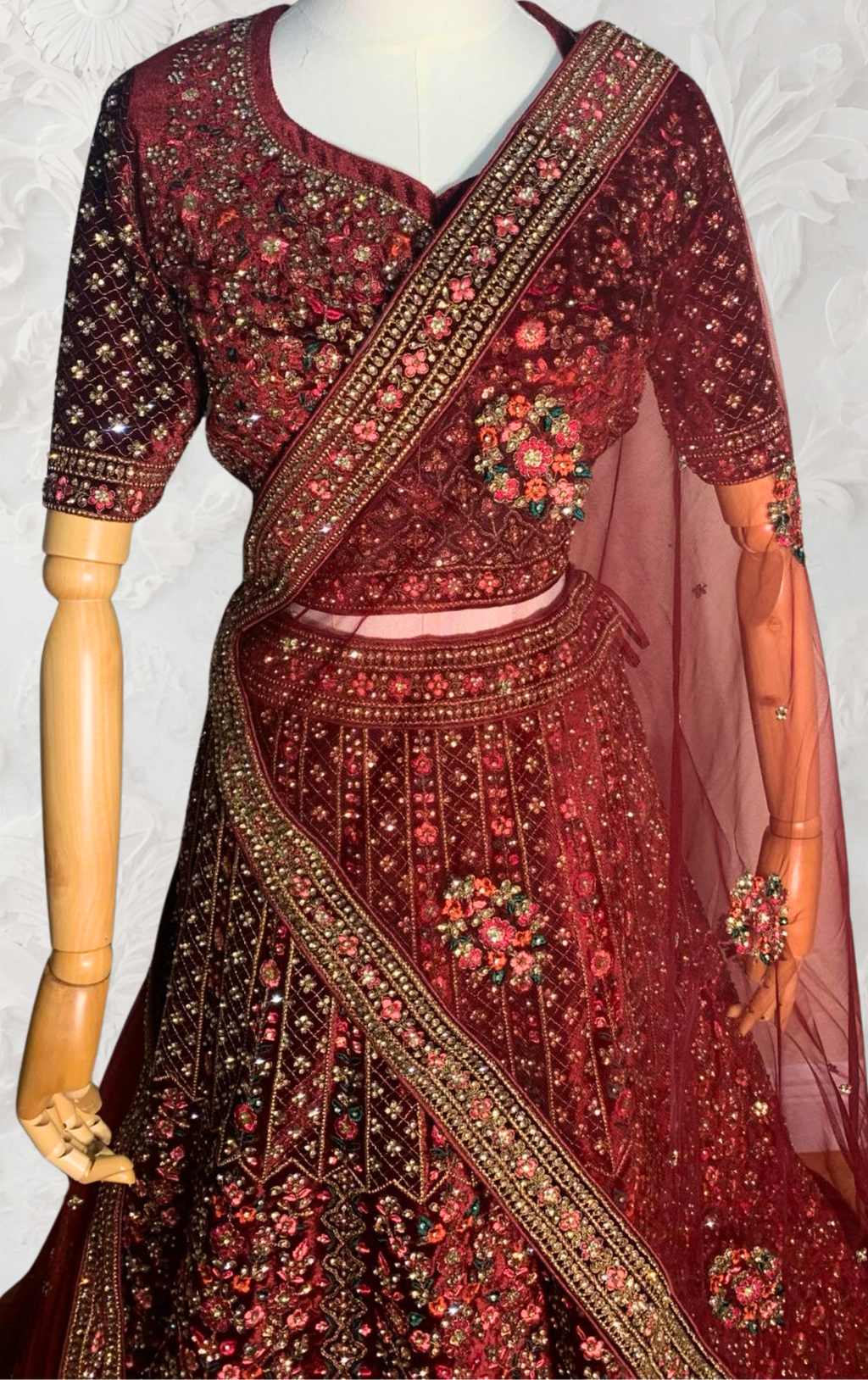 Maroon Lehenga with gold embroidery on a mannequin against a white wall. traditional desi, Indian, Pakistani, Bangladeshi, Sri lankan bridal ware for wedding. 