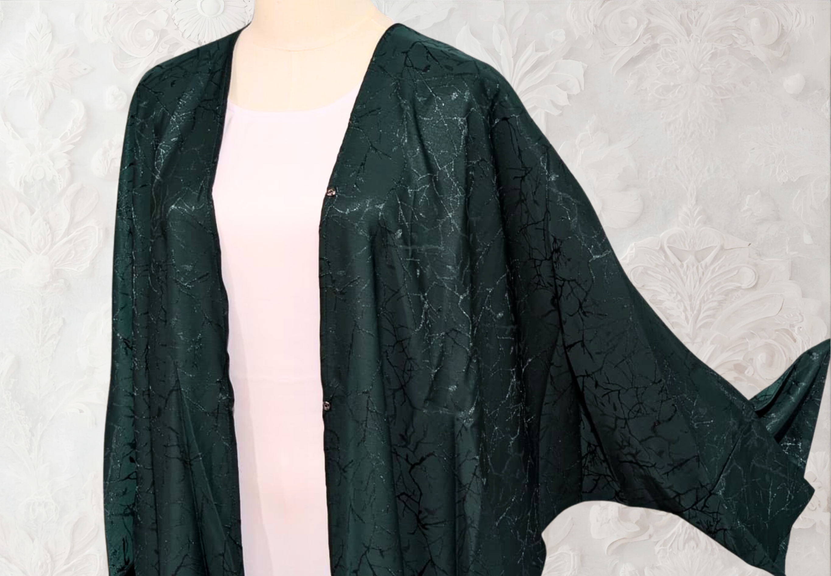 Mannequin wearing a dark green textured coat against a light textured wall.